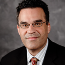 A man in a black suit and a red tie smiling